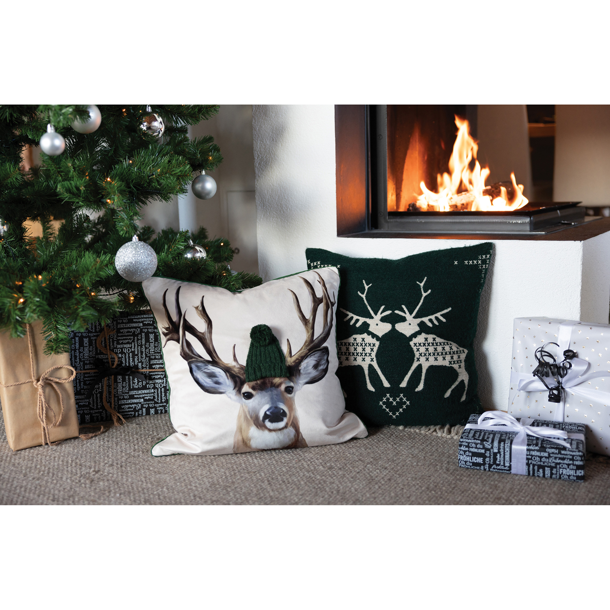 Kissenhülle Reindeer green im Szenebild dekriert vor einem Kamin mit anderen winterlichen Kissen und im Hintergrund ein Weihnachtsbaum