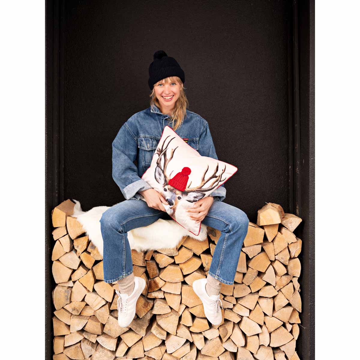 Mädel in Jeansjacke sitzend auf Holzstapel mit Reindeer-Kissen im Arm