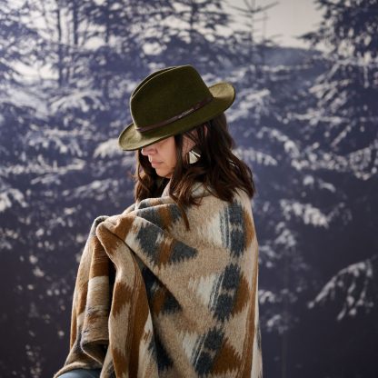 Frau mit Hut in Landschaft mit Bäumen stehend, umhüllt vom Plaid Sierra in Grau- und Beigetönen