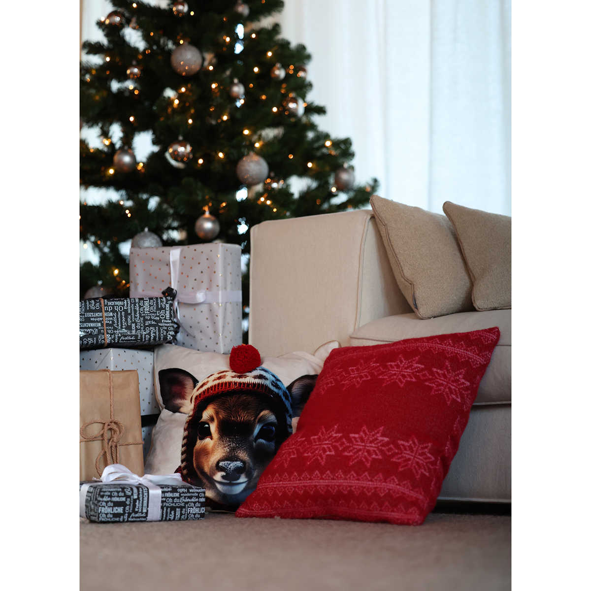 Kissenhülle Bambi vor einem Sofa stehend neben einem weiteren roten weihnachtlichen Kissen, im Hintergrund ein Weihnachtsbaum