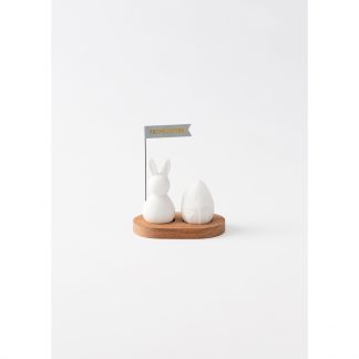 Hase sitzend mit Ei auf Holzsockel, Hase und Ei weißes unglasiertes Porzellan, Fähnchen grau mit rosa Aufschrift "Frohe Ostern"