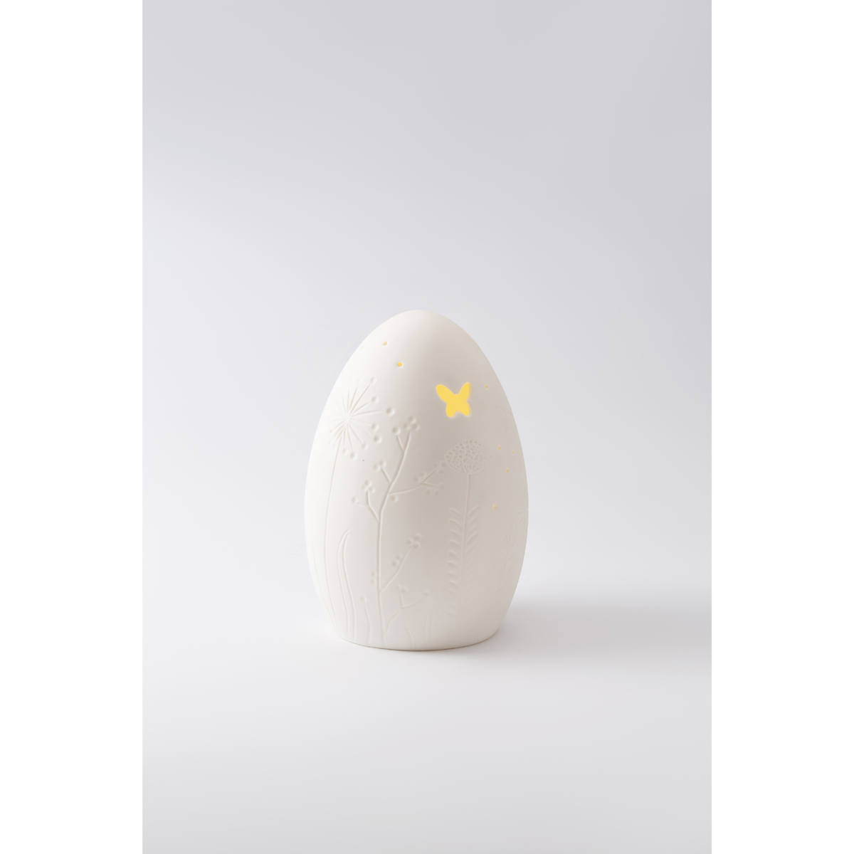 LED Leuchte aus weißem ungalsierten Porzellan in Eiform mit Relief von Blüten und Ranken und Aussparungen im Porzellan in Form von Punkten und einem Schmetterling, Lampe leuchtet, Muster Relief schimmert durch