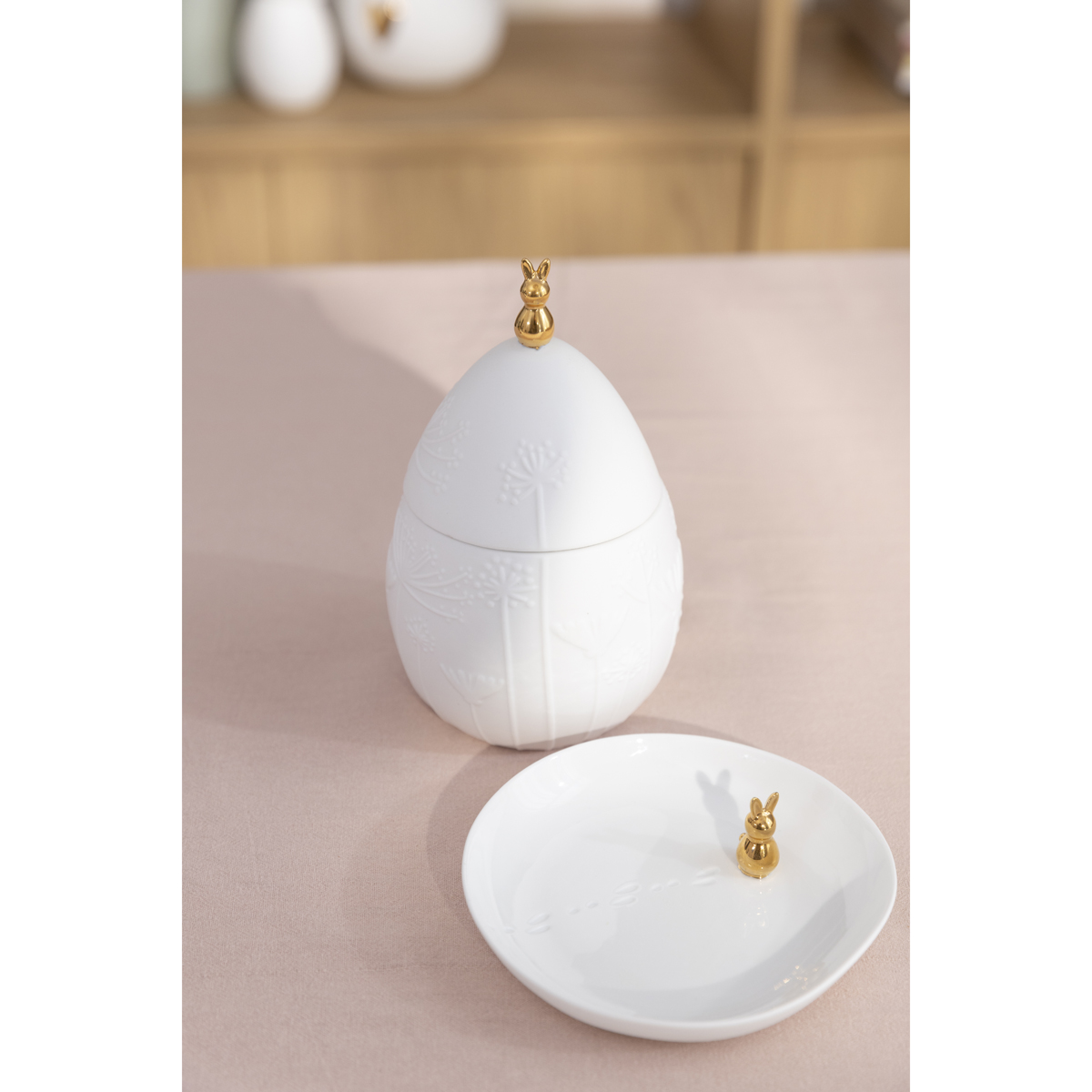 Osterdose in weiß mit klienem Ostertellerchen, ebf. weißes unglasiertes Porzellan, auf Tisch arrangiert